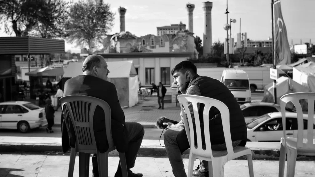 photo of two men sitting side by side talking to each other